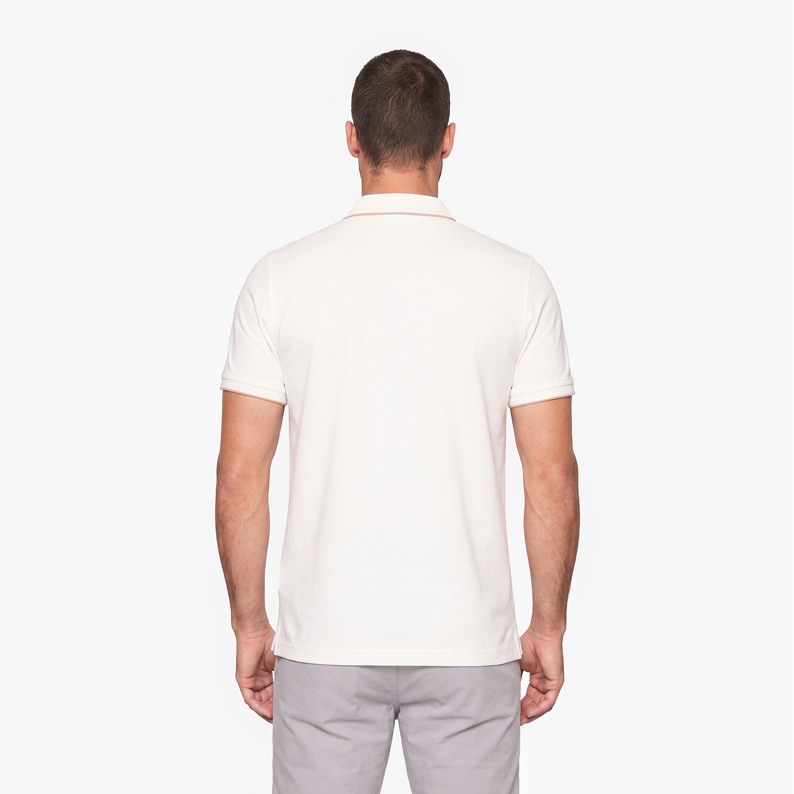 A man viewed from the back wearing a short-sleeve polo shirt in off-white and light gray trousers