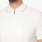 Close-up of a man wearing a cream-colored short-sleeve polo shirt with a half-zip collar and a small embroidered dog logo on the chest.