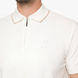 Close-up of a man wearing a cream-colored short-sleeve polo shirt with a half-zip collar and a small embroidered dog logo on the chest.