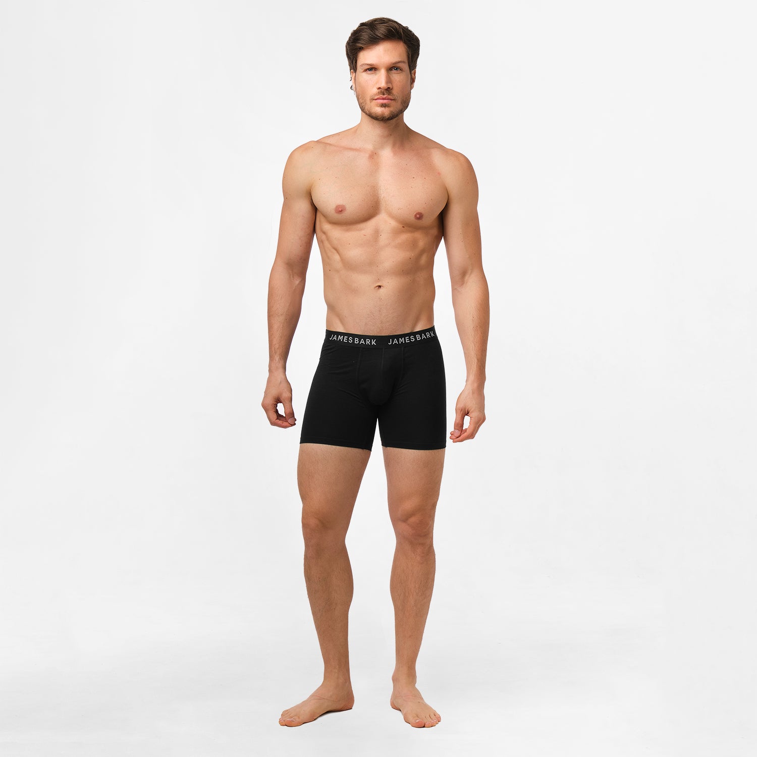 A man wearing black James Bark boxer briefs, standing against a plain white background. The waistband has 'JAMES BARK' branding in white letters, and the briefs have a snug fit.