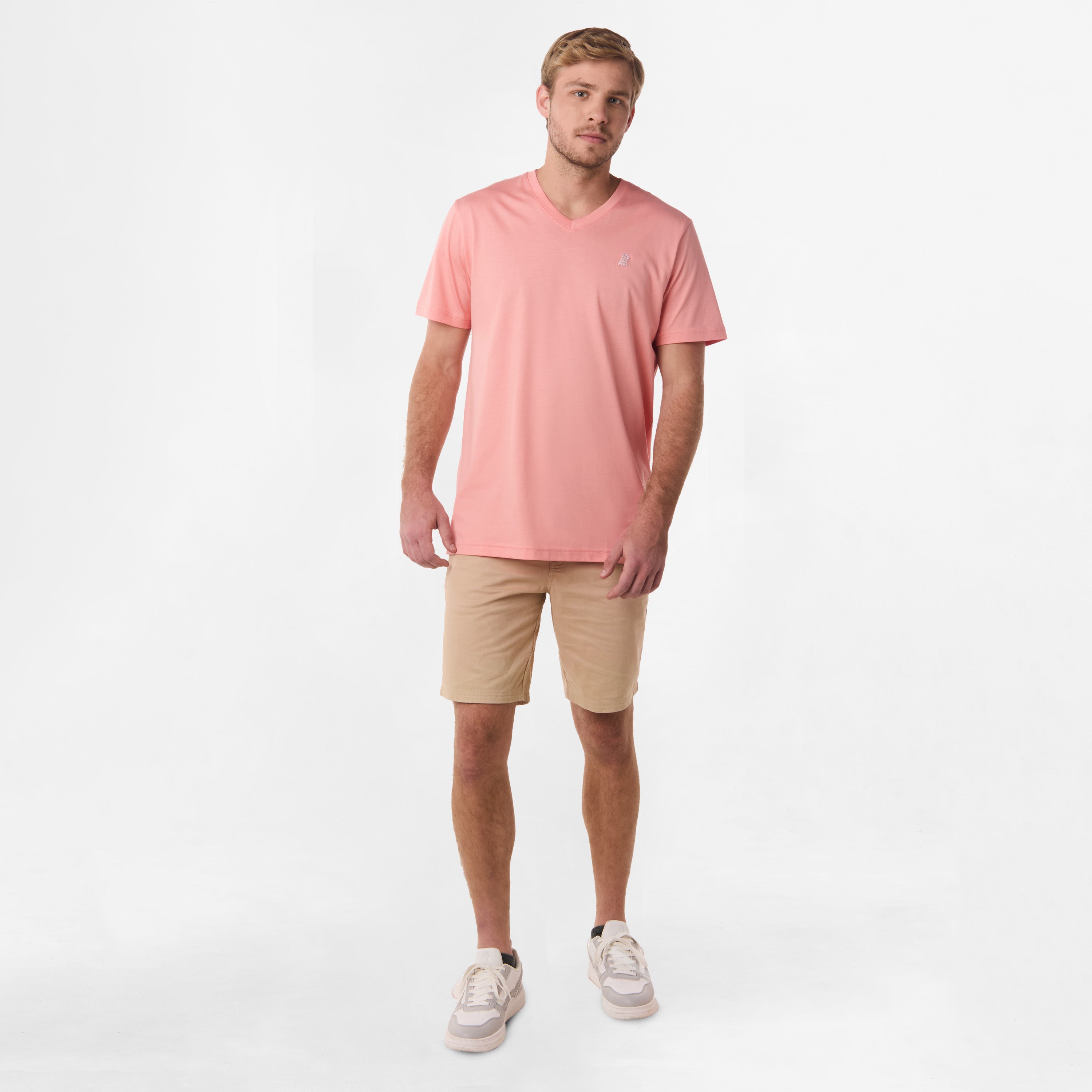 Full-body shot of the man wearing the coral V-neck t-shirt and beige shorts, standing with his hands relaxed by his sides.