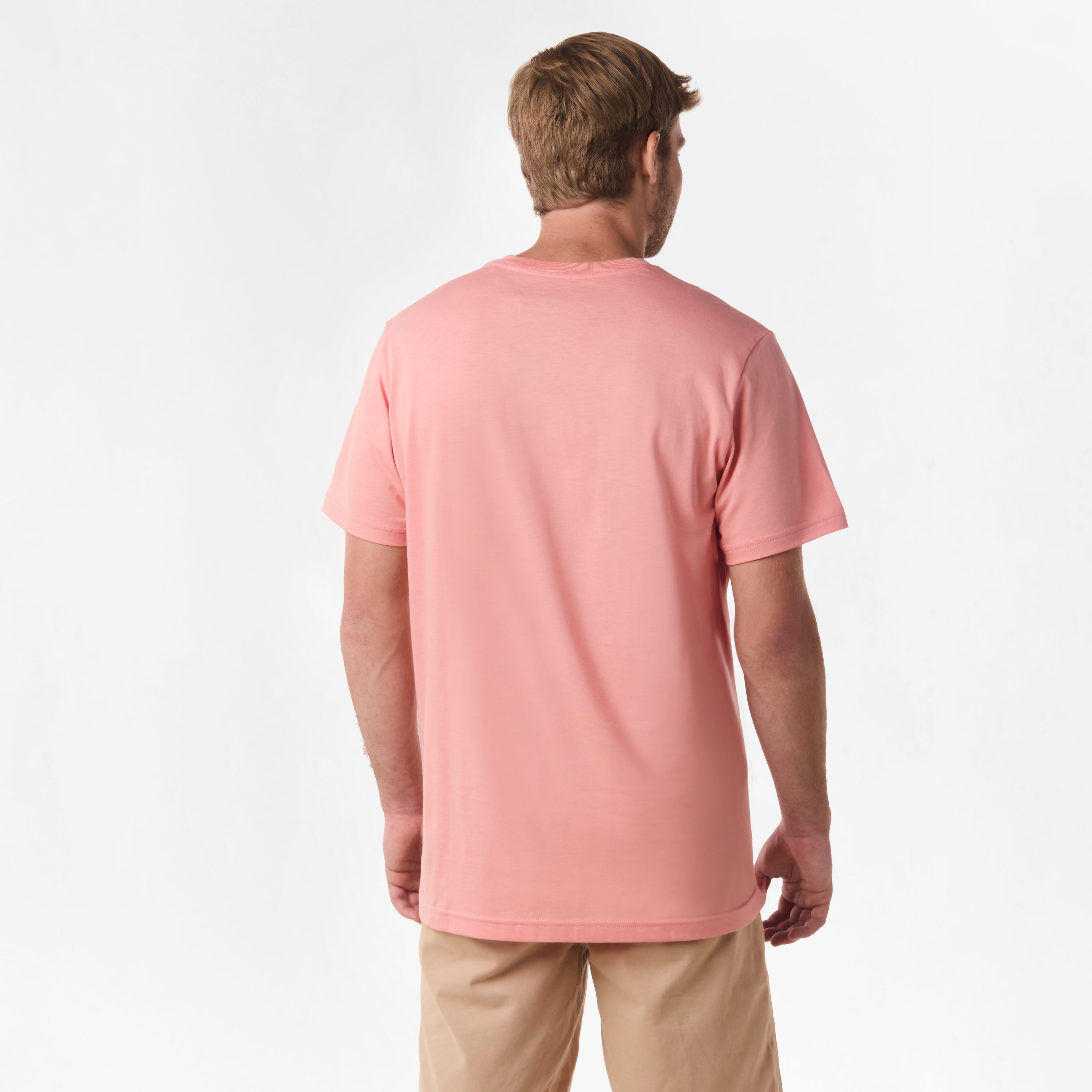 Rear view of the man wearing the coral V-neck t-shirt, showing the plain back design, paired with beige shorts.