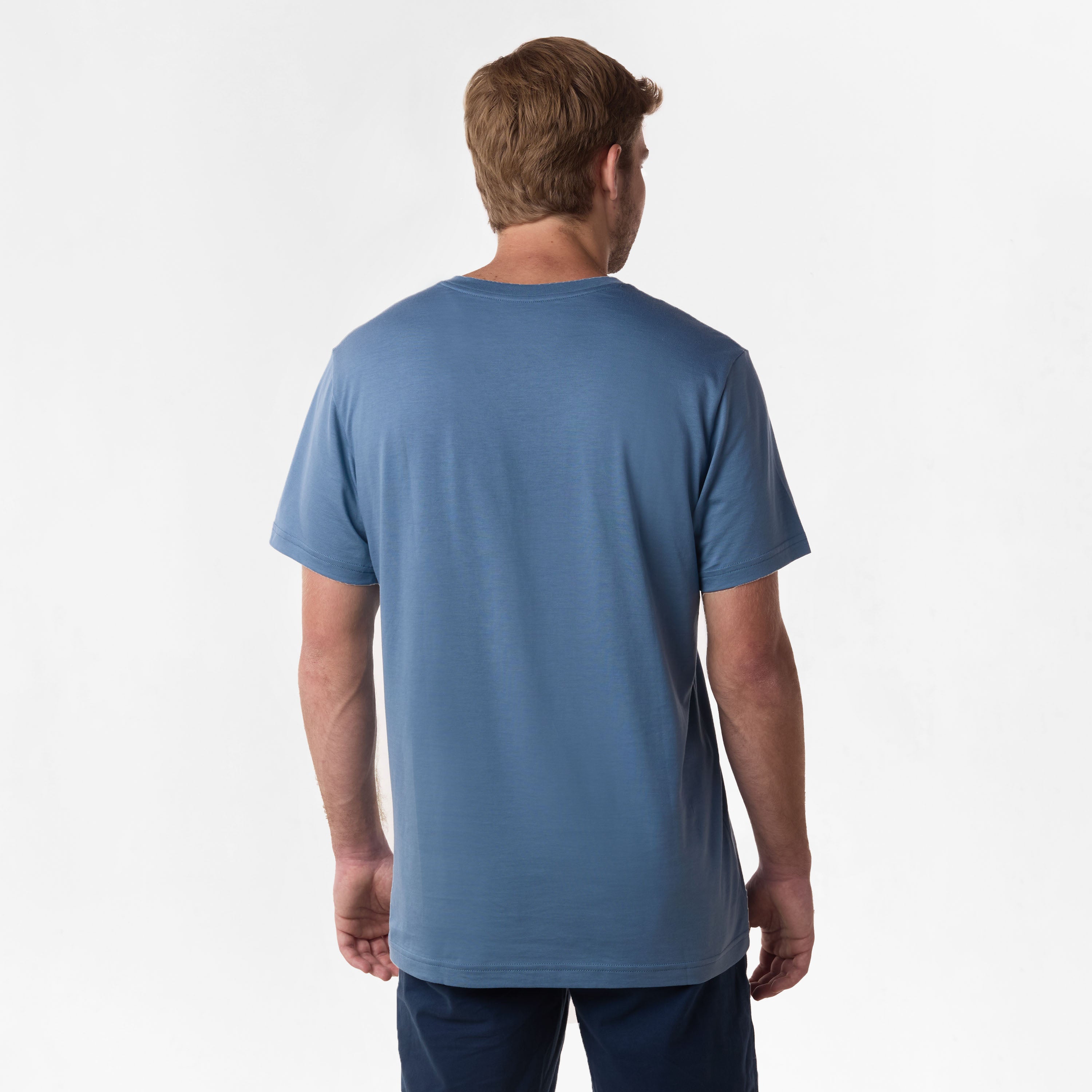 Rear view of the man wearing the blue V-neck t-shirt, showing the plain back design, paired with dark blue shorts.