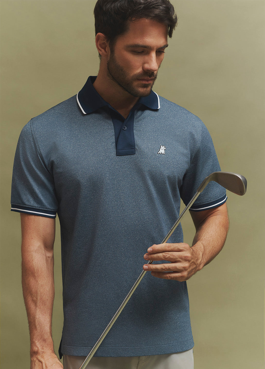 Man wearing a blue polo shirt holding a golf club against a green background