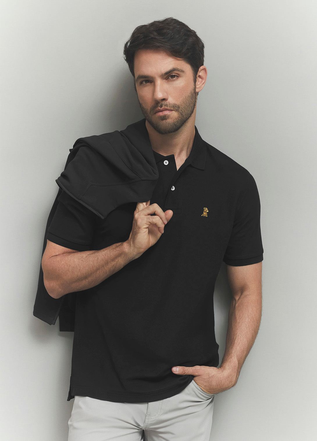 Man wearing a black polo shirt with a brand logo against a plain background