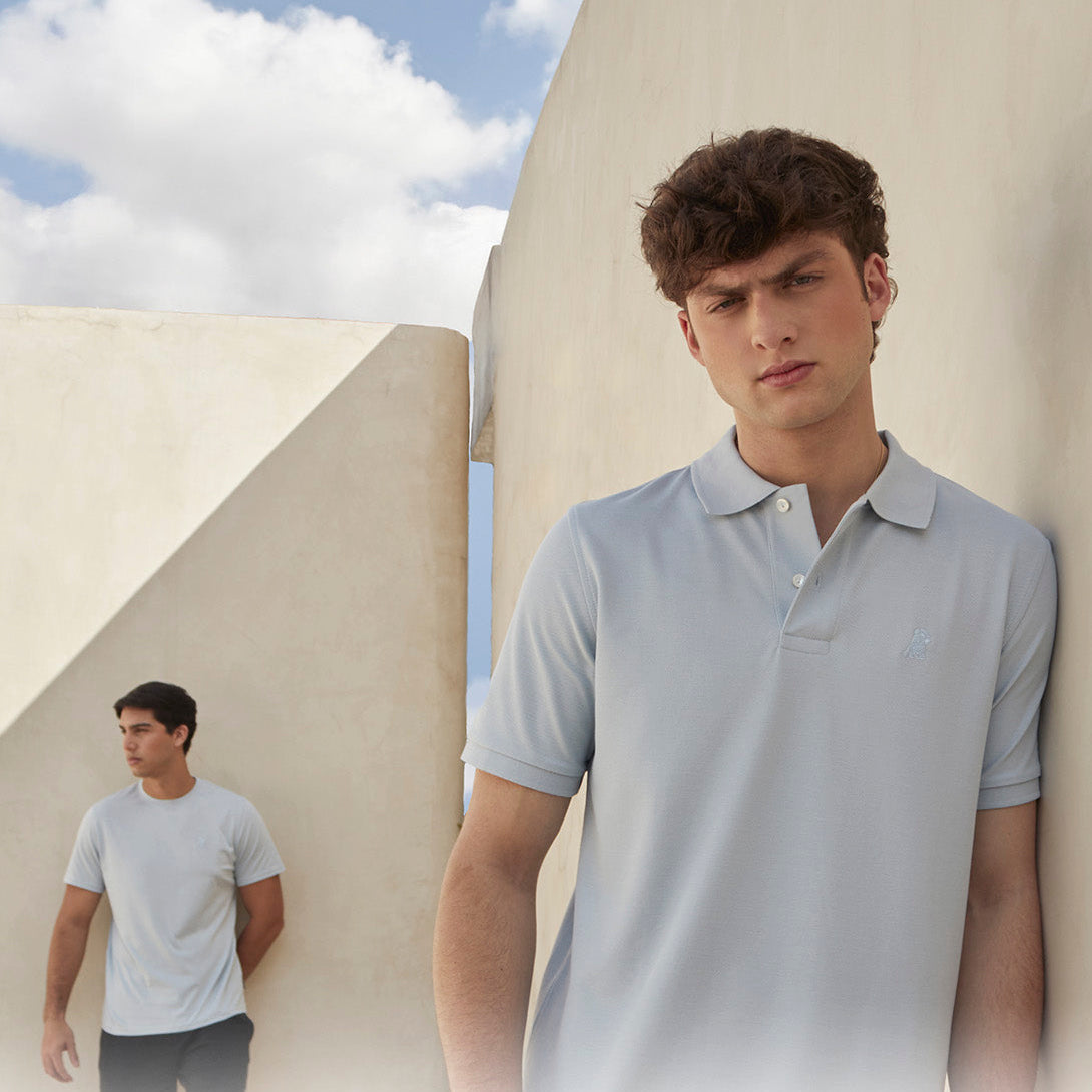 Man wearing a light gray polo shirt standing outdoors with a clear sky.