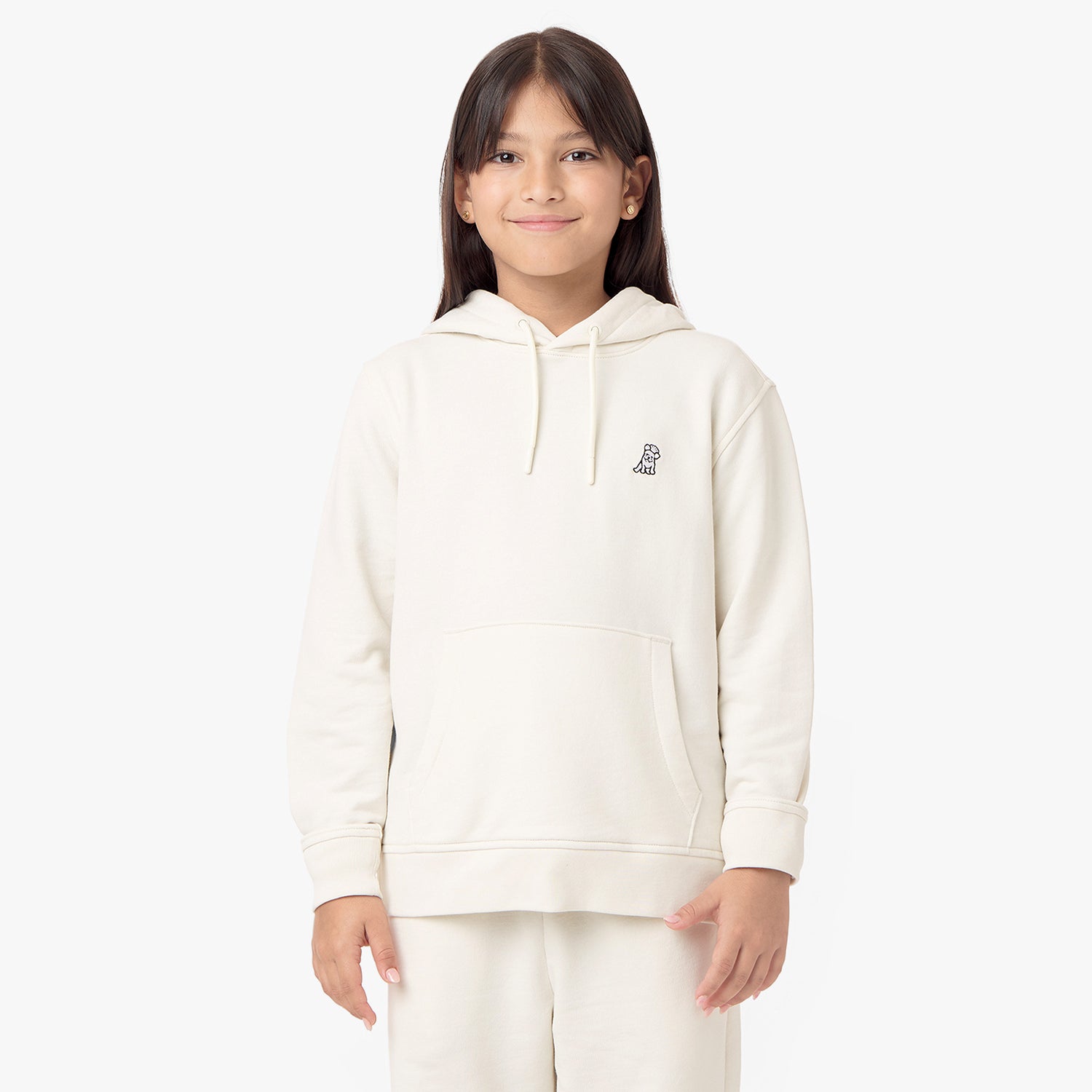 Front view of a child wearing a cream-colored hoodie with a small embroidered dog logo on the chest, smiling confidently.