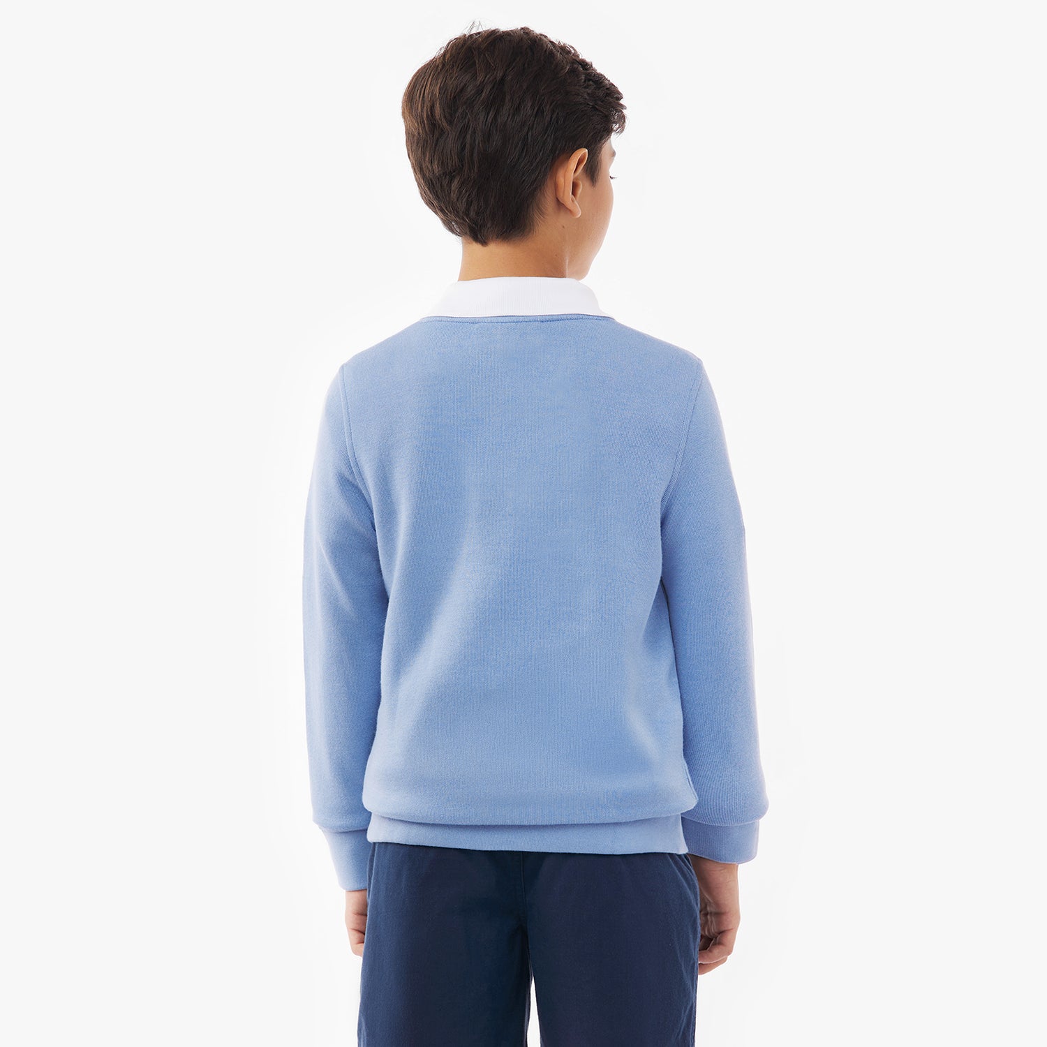 A young boy shown from the back, wearing a light blue sweatshirt over a white collared shirt and navy blue shorts. The background is plain white.