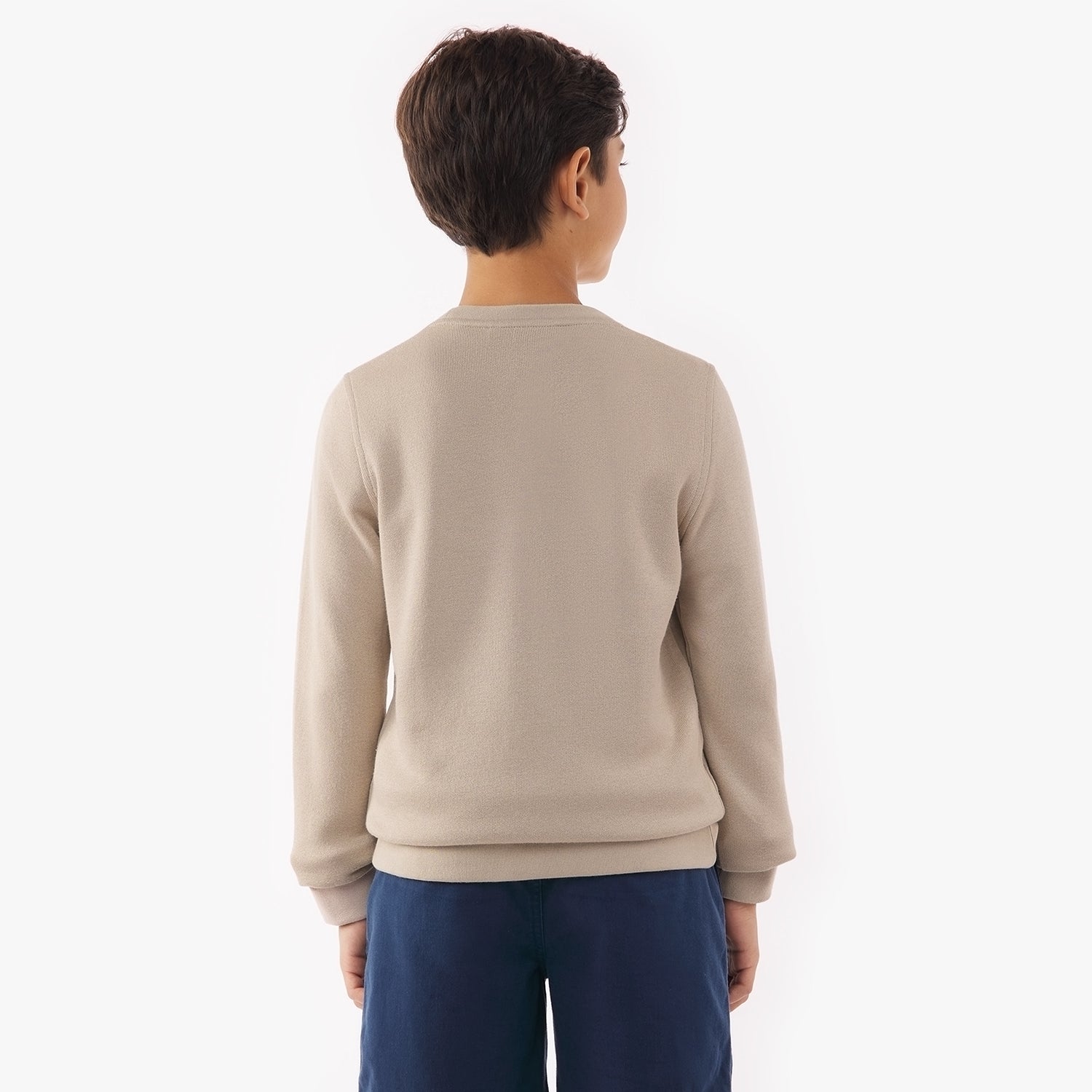 A young boy is shown from the back wearing a beige sweatshirt and navy blue shorts. His hands are at his sides, and the background is plain white.