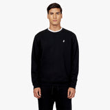 A model is wearing a black crewneck sweatshirt with a small embroidered logo on the left chest. The sweatshirt is paired with matching black joggers featuring a drawstring waist. The overall look is simple, minimalist, and casual