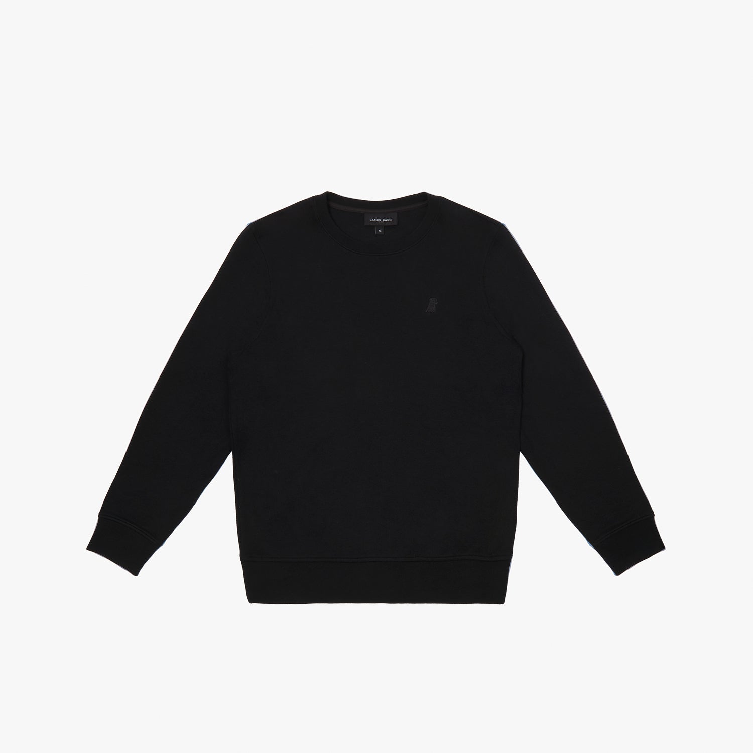 A black crewneck sweatshirt laid flat on a white background. It features long sleeves, ribbed cuffs, and a ribbed hem. A subtly embroidered logo, matching the black fabric, is positioned on the left chest area. The neckline includes a black label with white text displaying the brand "JAMES BARK." The fabric appears soft and comfortable.