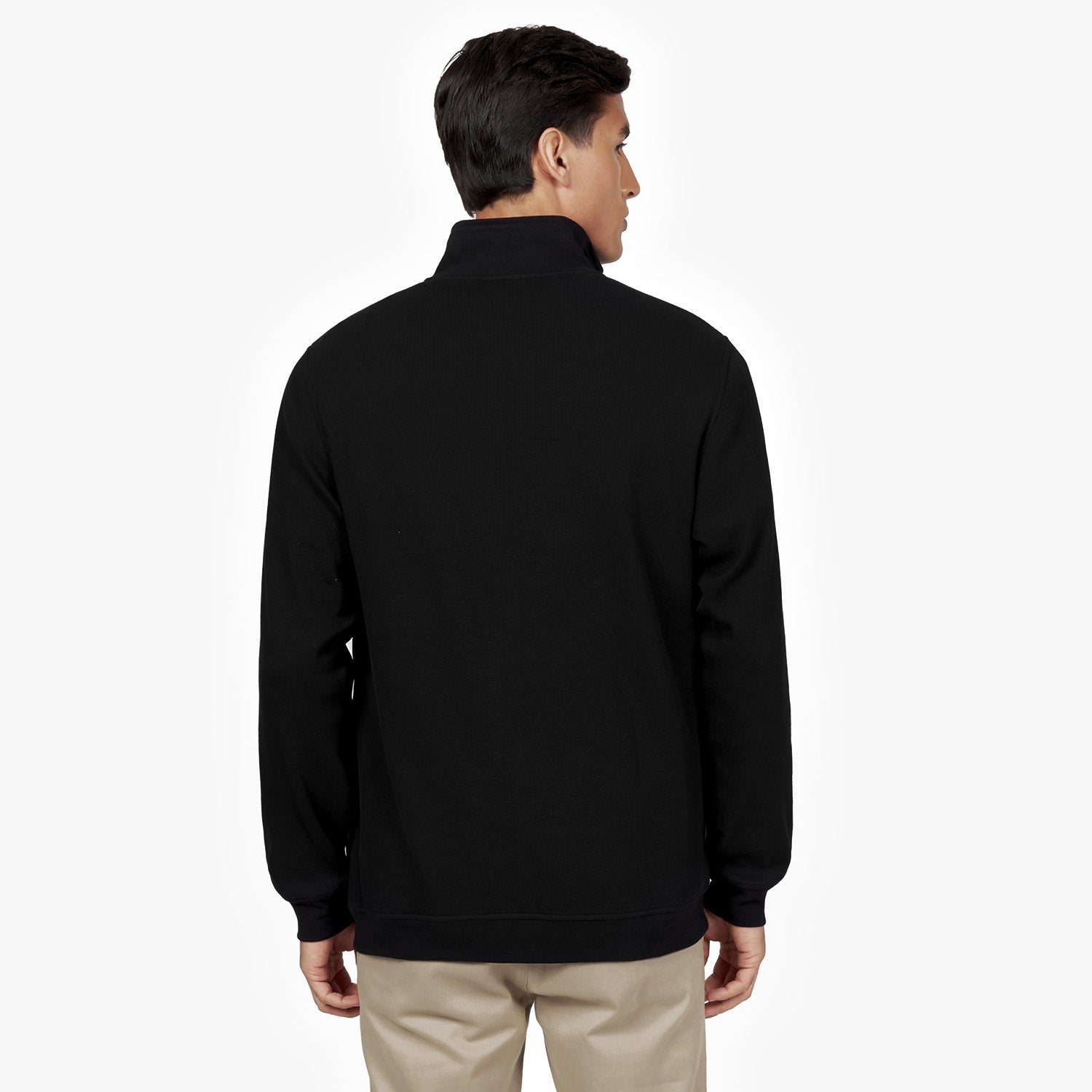 Back view of a man wearing a black half-zip sweatshirt with a high collar. The sweatshirt has a clean, minimalist design. He is also wearing beige pants. The background is plain white