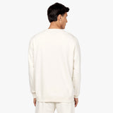 Back view of a man wearing an off-white crewneck sweatshirt paired with matching off-white sweatpants. The sweatshirt has a clean, minimalist design with no visible logos or patterns on the back, maintaining a sleek and simple style