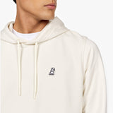 Close-up of a man wearing an off-white hoodie featuring an embroidered black and white dog logo on the chest. The hoodie has drawstrings and is paired with a white T-shirt underneath, displayed against a plain white background." Let me know if you'd like any adjustments