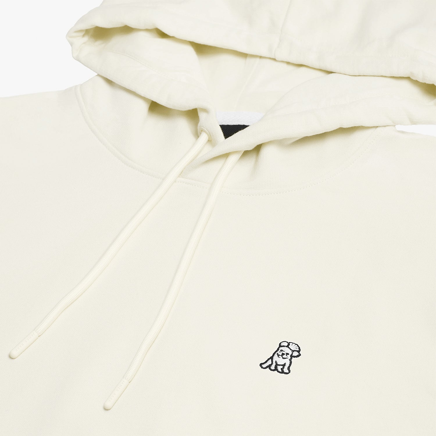 Close-up of the embroidered dog logo on the chest of the cream-colored hoodie, highlighting the fine details