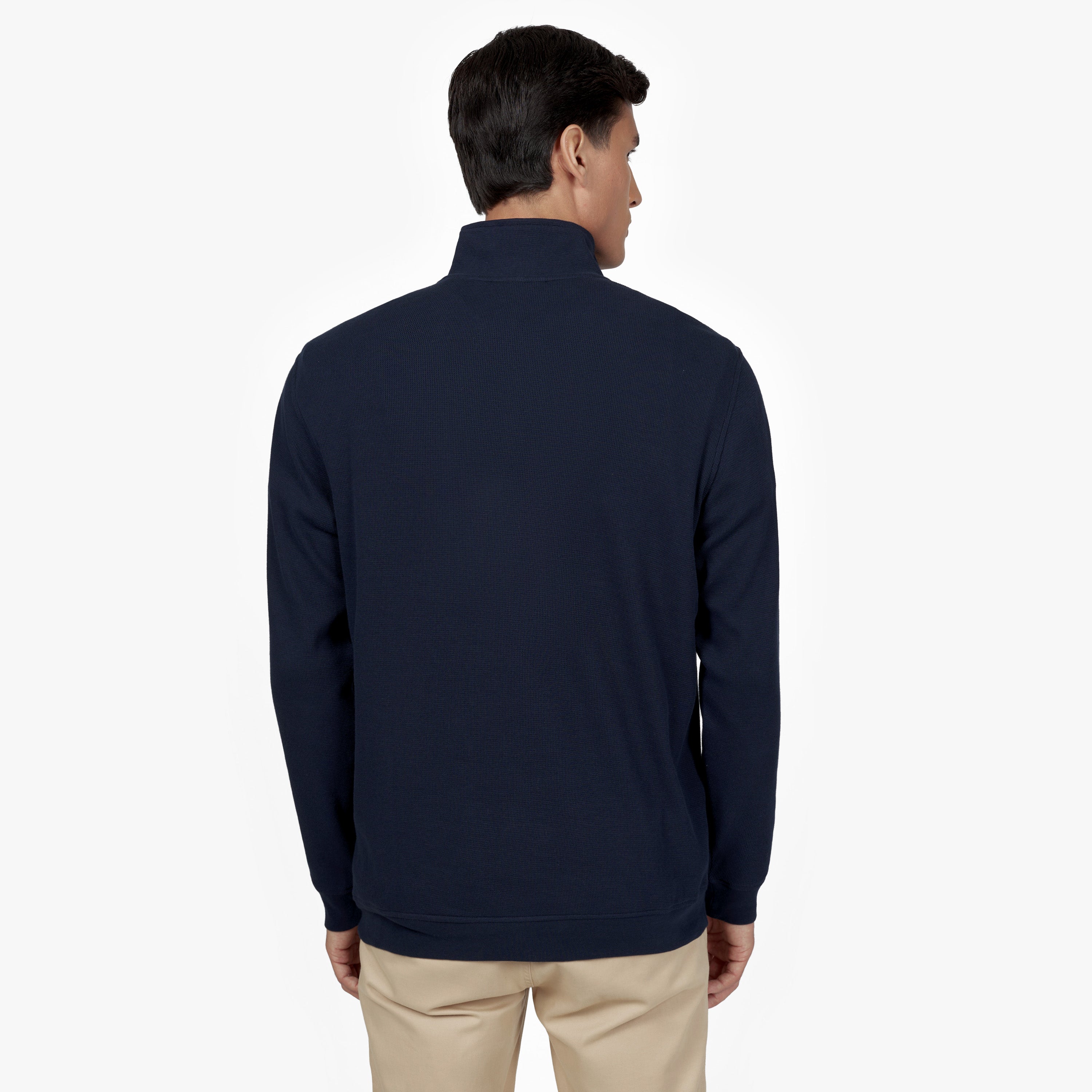 "Back view of a man wearing a navy blue half-zip sweatshirt with a high collar. The sweatshirt has a clean, minimalist design. He is also wearing beige pants. The background is plain white