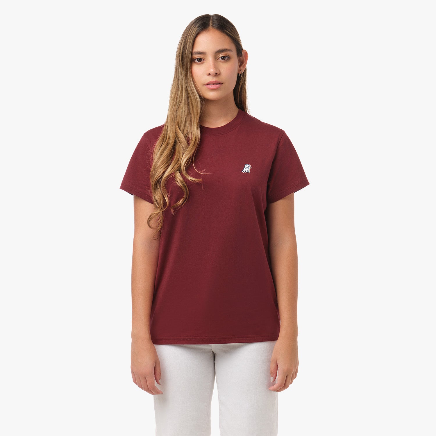 A woman stands facing forward, wearing a maroon T-shirt with a small dog logo on the chest and white pants. She has a neutral expression.