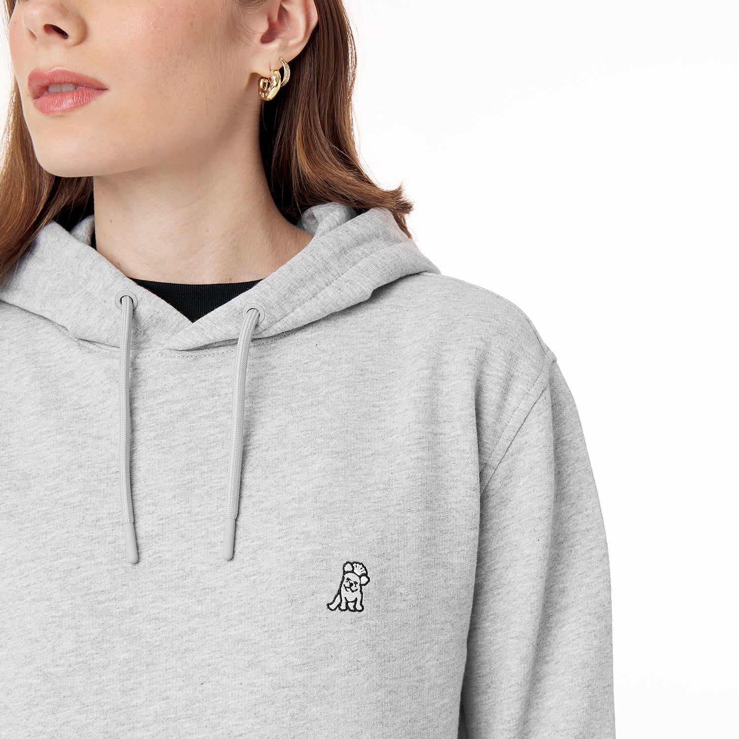 Close-up of a person wearing a light gray hoodie with a small embroidered dog logo on the chest. The person has light skin, long brown hair, and is wearing gold hoop earrings, with a plain white background." Let me know if you'd like adjustments!