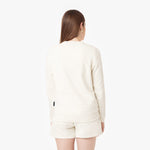 Rear view of a woman wearing an off-white crewneck sweatshirt and matching shorts, showcasing the simple and minimal back design. The outfit exudes a casual and comfortable style.