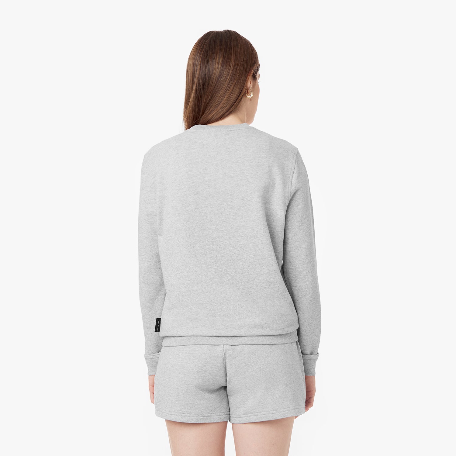 Back view of a woman wearing a light gray sweatshirt and matching shorts set, showcasing the simple and clean design of the outfit.