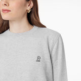 Close-up of a woman wearing a light gray sweatshirt, focusing on the embroidered dog logo on the chest and her gold hoop earrings.