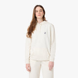 Woman wearing an off-white hoodie with a small embroidered graphic on the chest. She is styled with matching off-white pants, loose wavy hair, and gold hoop earrings, posing against a plain white background.