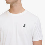 A close-up of a man wearing a white T-shirt with a small black embroidered dog logo on the left chest