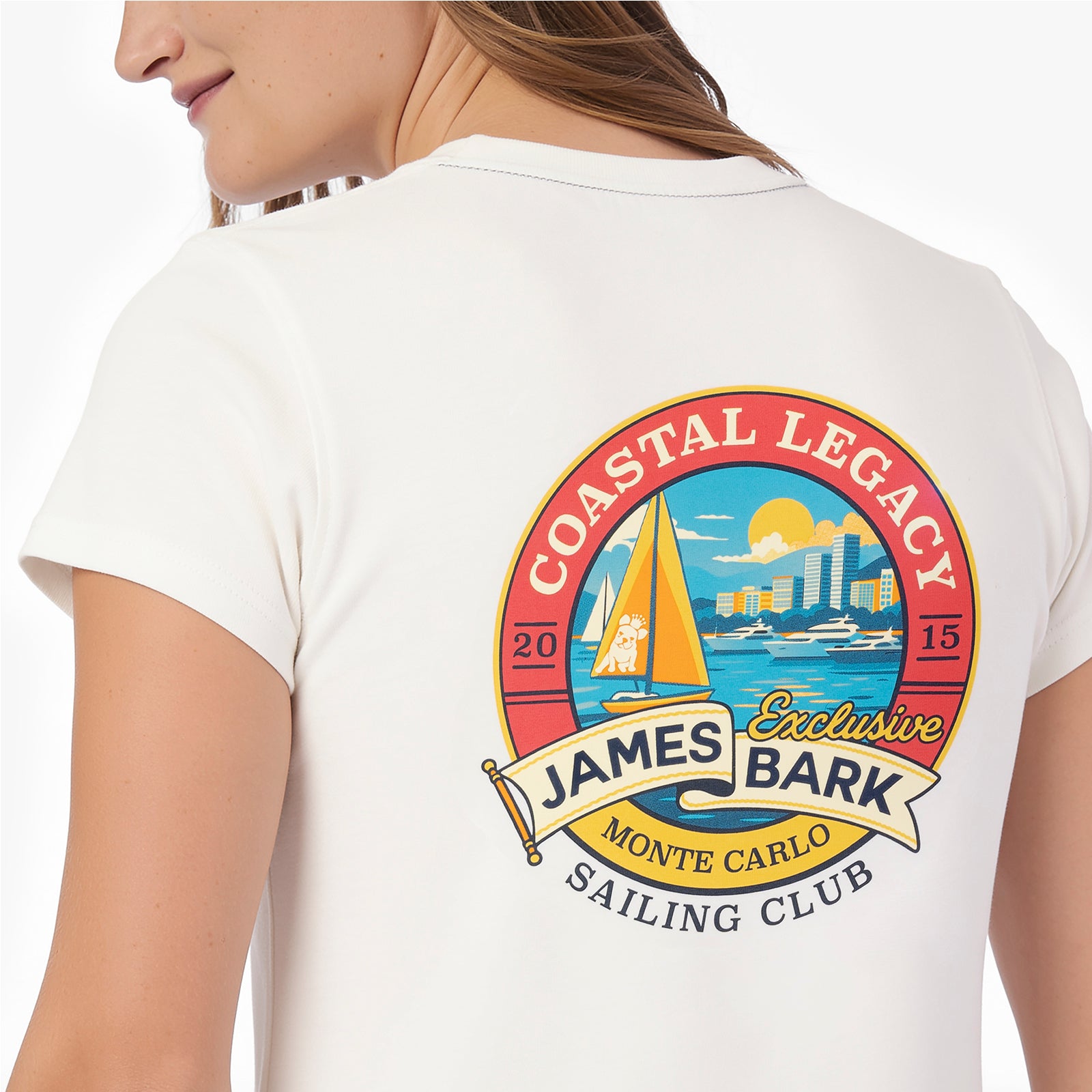 A woman is shown from the back wearing a white T-shirt with a large, colorful circular graphic on the back. The graphic includes the text 'COASTAL LEGACY', 'JAMES BARK', 'MONTE CARLO', and 'SAILING CLUB' around a sailboat scene.