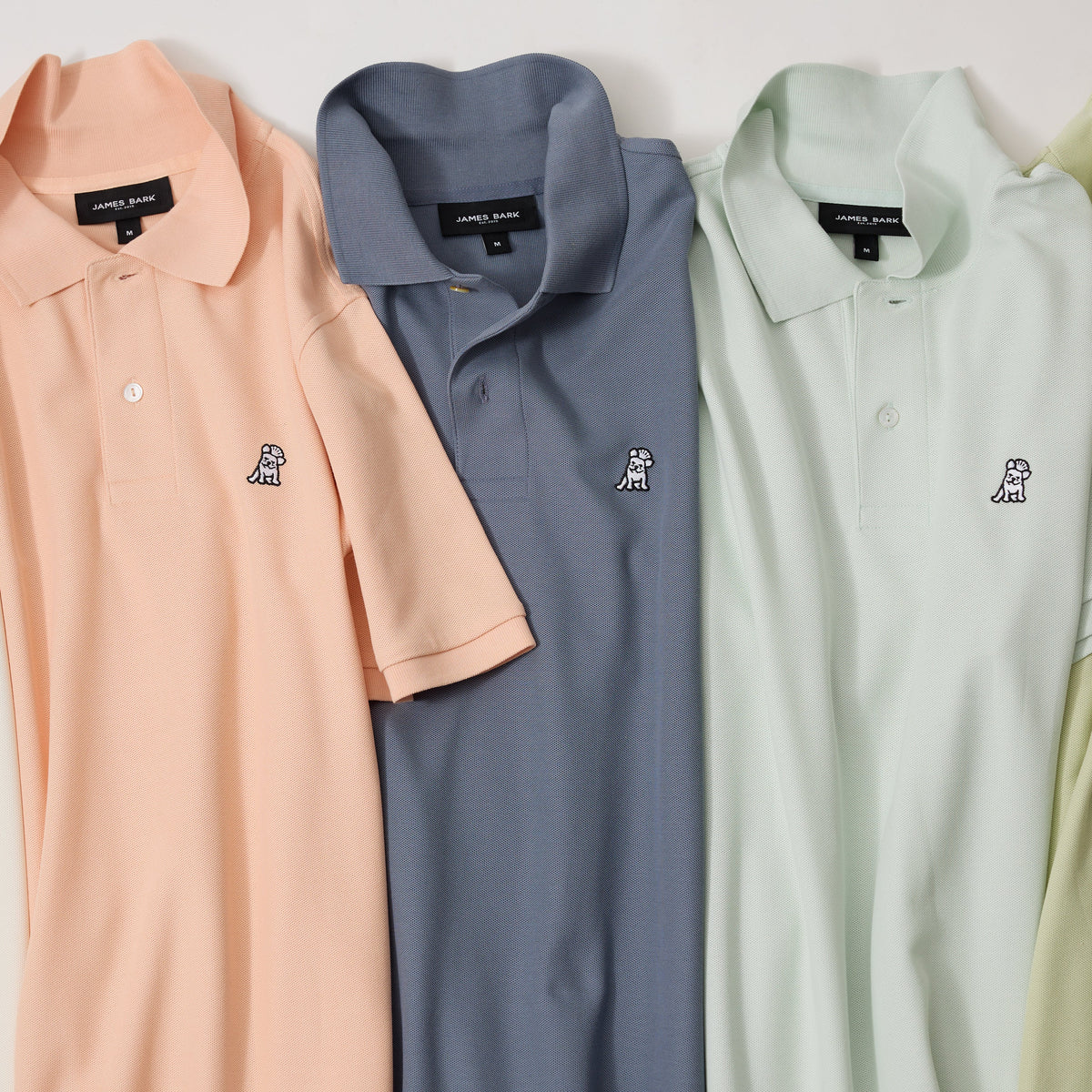 Stack of folded James Bark polo shirts in pastel colors, highlighting the embroidered Frenchie logo detail on each