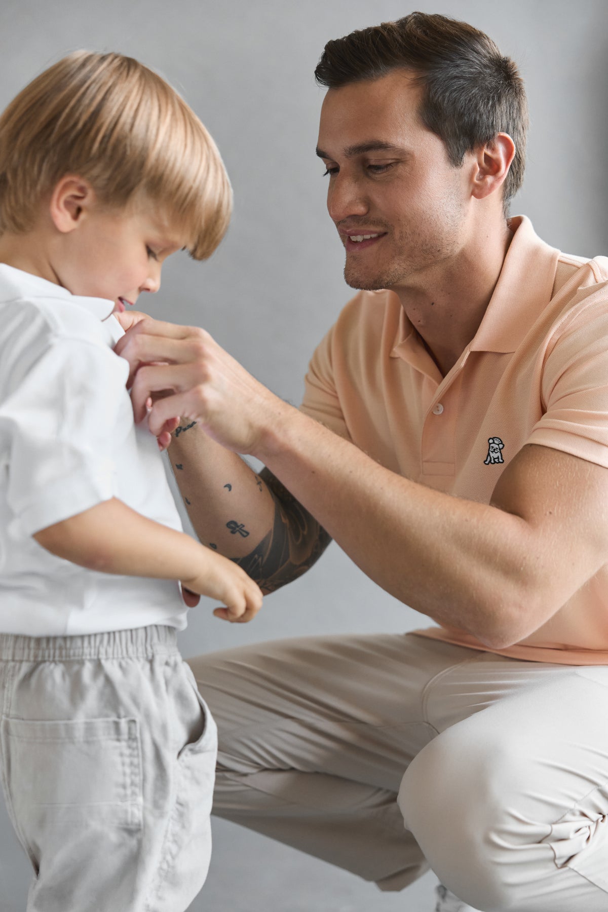 A man wearing a peach color polo shirt with a little boy wearing a white polo shirt