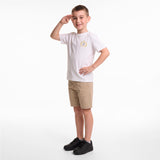 A young boy modeling a white short-sleeve T-shirt with a small gold crest on the left chest, paired with khaki shorts and black sneakers