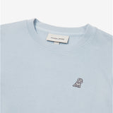 A close-up of a light pastel blue crewneck sweatshirt, showing the ribbed collar and finely knit fabric texture. The white neck label displays the brand name "JAMES BARK" with "Est. 2015" beneath it. A small embroidered logo of a dog in dark thread is positioned on the left chest area, standing out against the light fabric. The material appears soft and high-qua