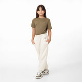 Young model wearing an olive green T-shirt paired with off-white jogger pants, featuring a small embroidered logo on both garments. The outfit is completed with green and white sneakers, styled casually with hands in pockets.