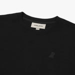 A close-up of a black crewneck sweatshirt, showing the ribbed collar and finely knit fabric texture. The white neck label displays the brand name "JAMES BARK" with "Est. 2015" beneath it. A subtly embroidered logo of a dog, matching the black fabric, is positioned on the left chest area. The material appears soft and high-quality.