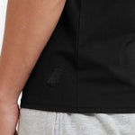 Black t-shirt with a logo on the chest worn by a person, with gray shorts visible.