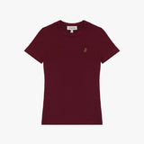 A burgundy short-sleeve T-shirt laid flat on a white background. It features a ribbed crewneck collar and a fitted silhouette. A small embroidered logo of a dog in a slightly darker shade is positioned on the left chest area. The neckline includes a white label with black text displaying the brand "JAMES BARK" and the size "S." The fabric appears soft and high-quality.