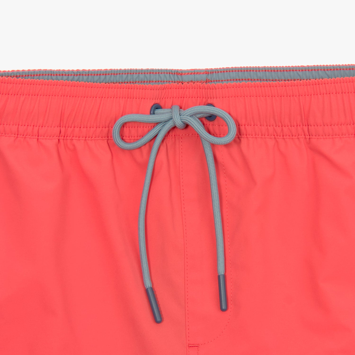 Close-up of the contrasting drawstring on the waistband of the coral-colored swim trunks, tied in a neat bow.