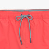 Close-up of the contrasting drawstring on the waistband of the coral-colored swim trunks, tied in a neat bow.