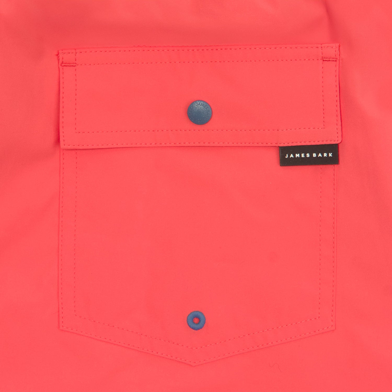 Detailed view of the back pocket of the coral-colored swim trunks, highlighting a snap button and embroidered brand label.