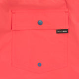 Detailed view of the back pocket of the coral-colored swim trunks, highlighting a snap button and embroidered brand label.