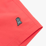 Close-up of the embroidered brand logo on the hem of the coral-colored swim trunks, emphasizing its distinctive design.