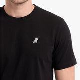 A close-up of a man wearing a black short-sleeve crewneck t-shirt with a small white embroidered dog