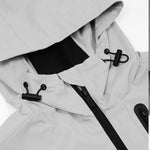 Close-up of the hood area of a light gray jacket, featuring adjustable black drawstrings with toggle locks on each side. The jacket has a black zipper at the front, with a sleek and functional design. The stitching is precise, and the fabric appears durable, highlighting the jacket’s practicality.