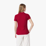 Back of woman wearing a red polo shirt and white pants on a white background