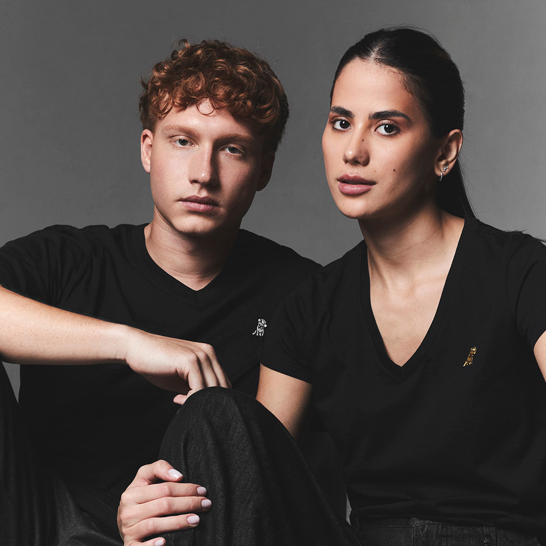 Two people sitting side by side wearing black outfits with a neutral background