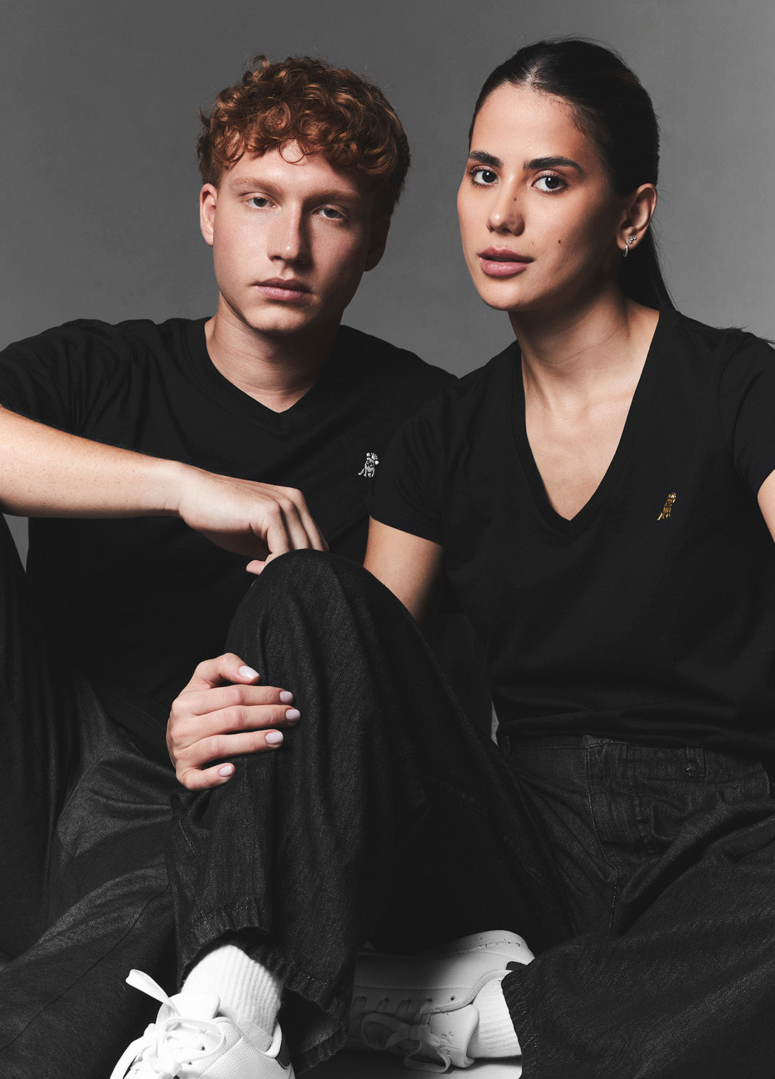Two people sitting side by side wearing black outfits with a neutral background