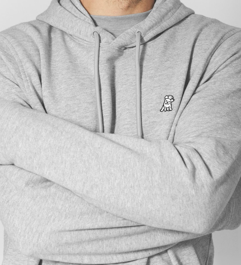 Person wearing a gray french terry hoodie with a small logo on a plain background