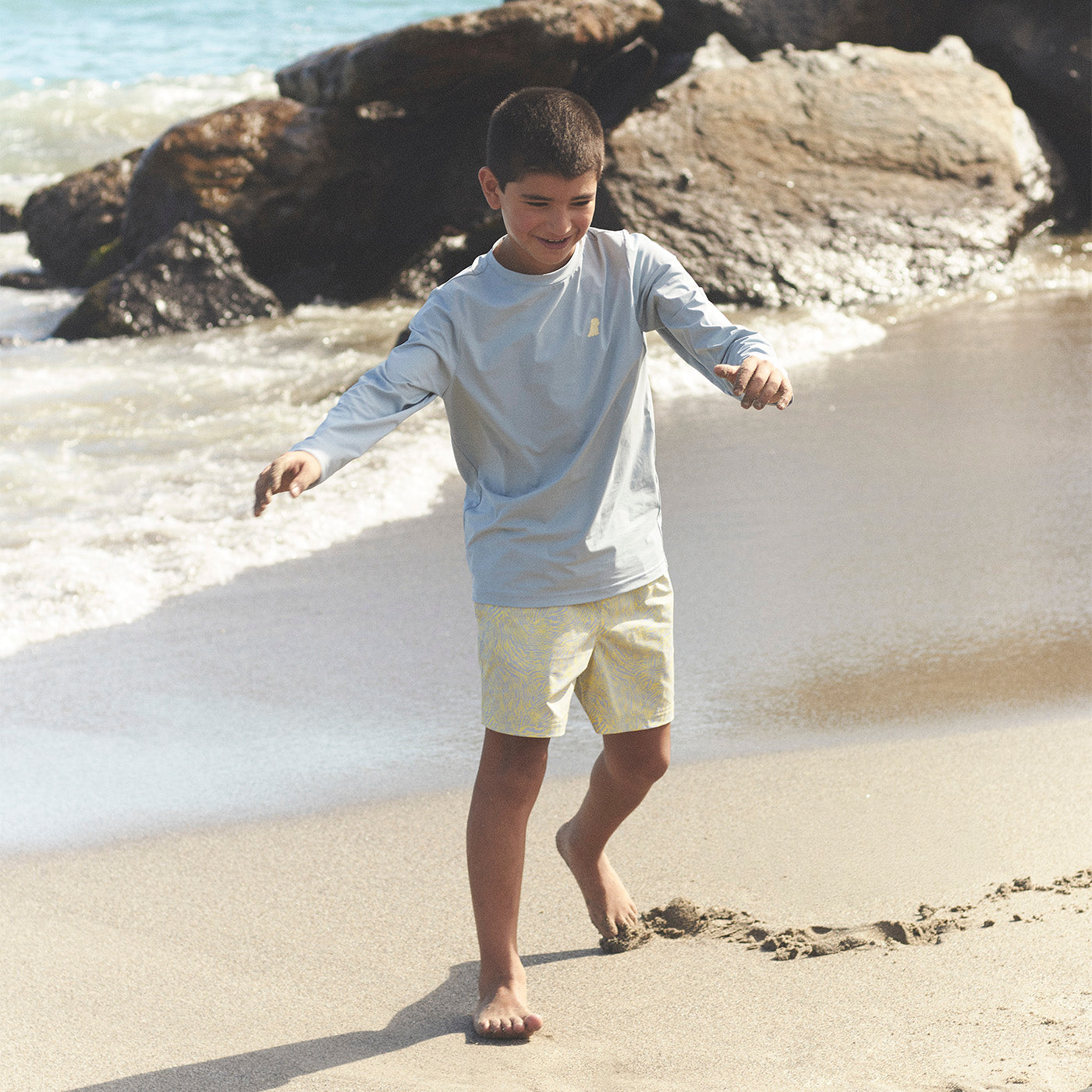 Young boy playing on a beach with waves and rocks in the background