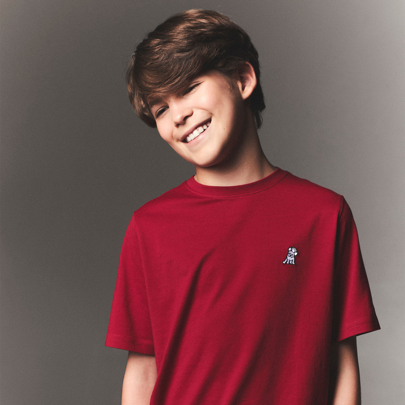 Young person wearing a red t-shirt with a small logo on a gray background