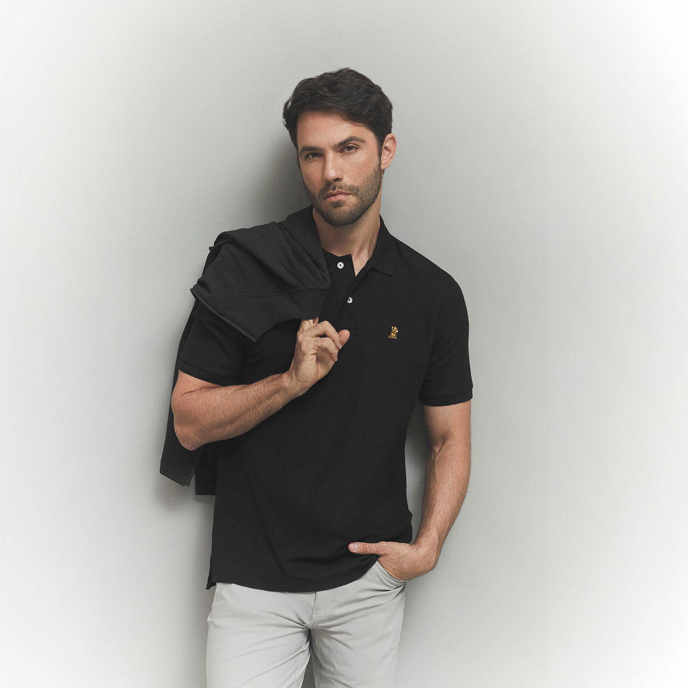 Man wearing a black polo shirt with a logo against a light gray background